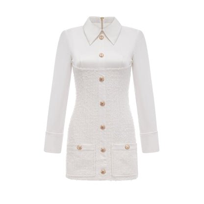 A woman wearing a white mini dress with short sleeves and a single row of buttons down the front standing against a plain background