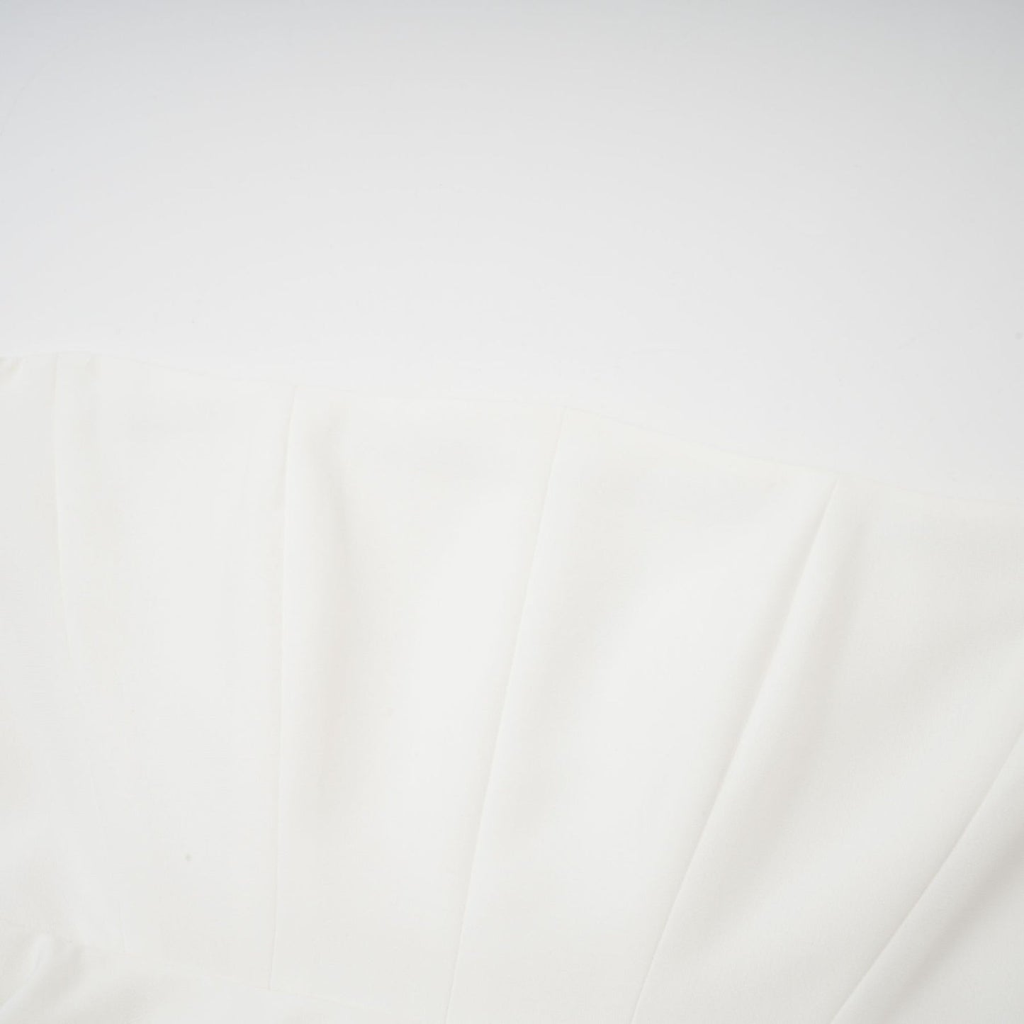 A woman wearing a white offshoulder maxi dress with pleated details standing against a plain background
