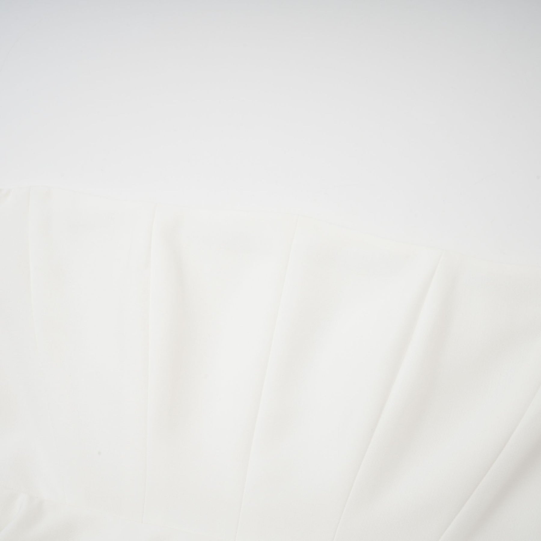 A woman wearing a white offshoulder maxi dress with pleated details standing against a plain background