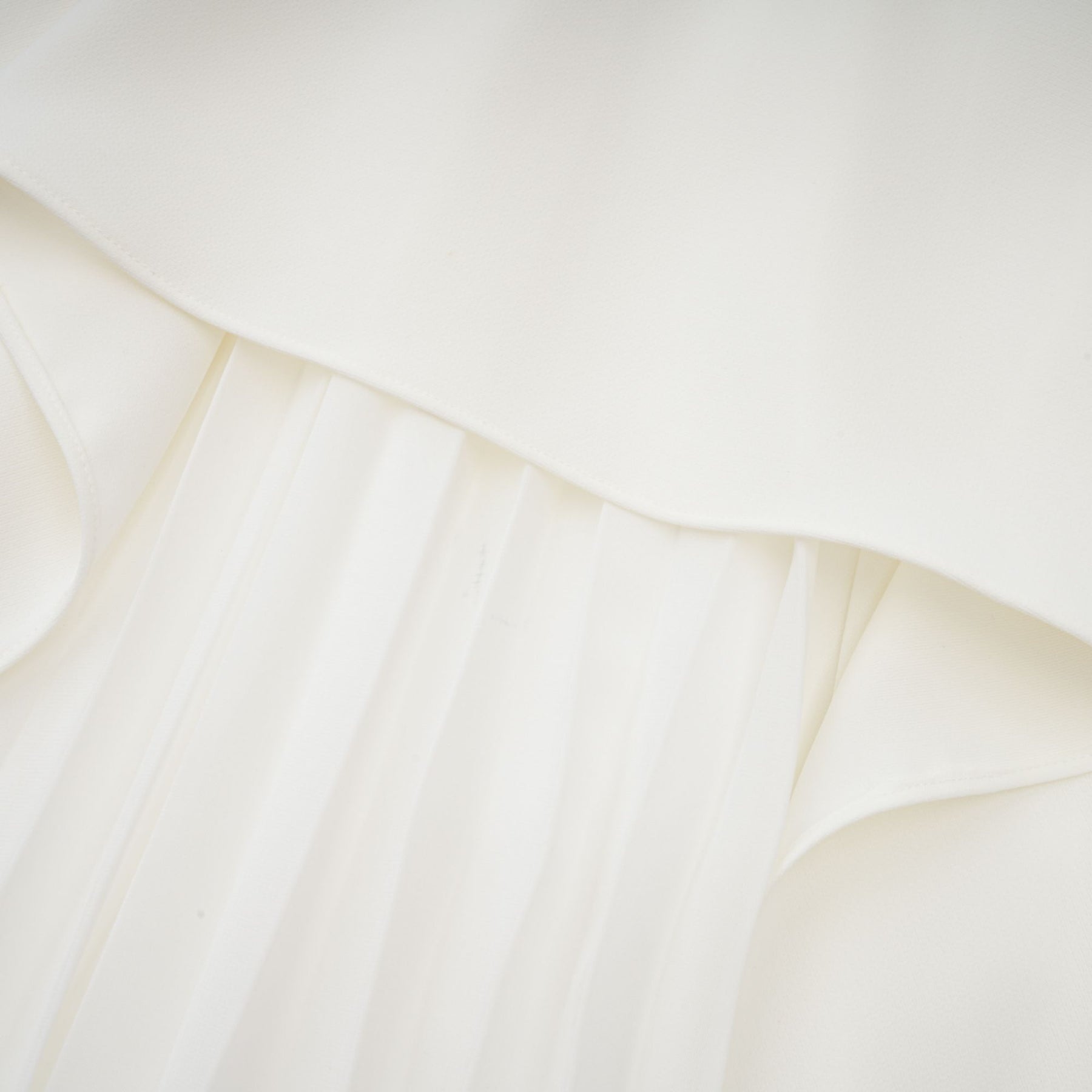 A woman wearing a white offshoulder maxi dress with pleated details the dress has a flowy silhouette and extends to the floor