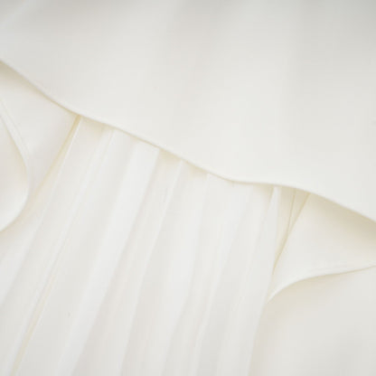 A woman wearing a white offshoulder maxi dress with pleated details the dress has a flowy silhouette and extends to the floor