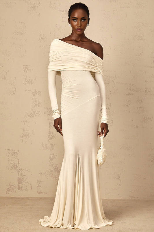 A woman wearing a white offshoulder maxi dress with ruched detailing standing in a relaxed pose