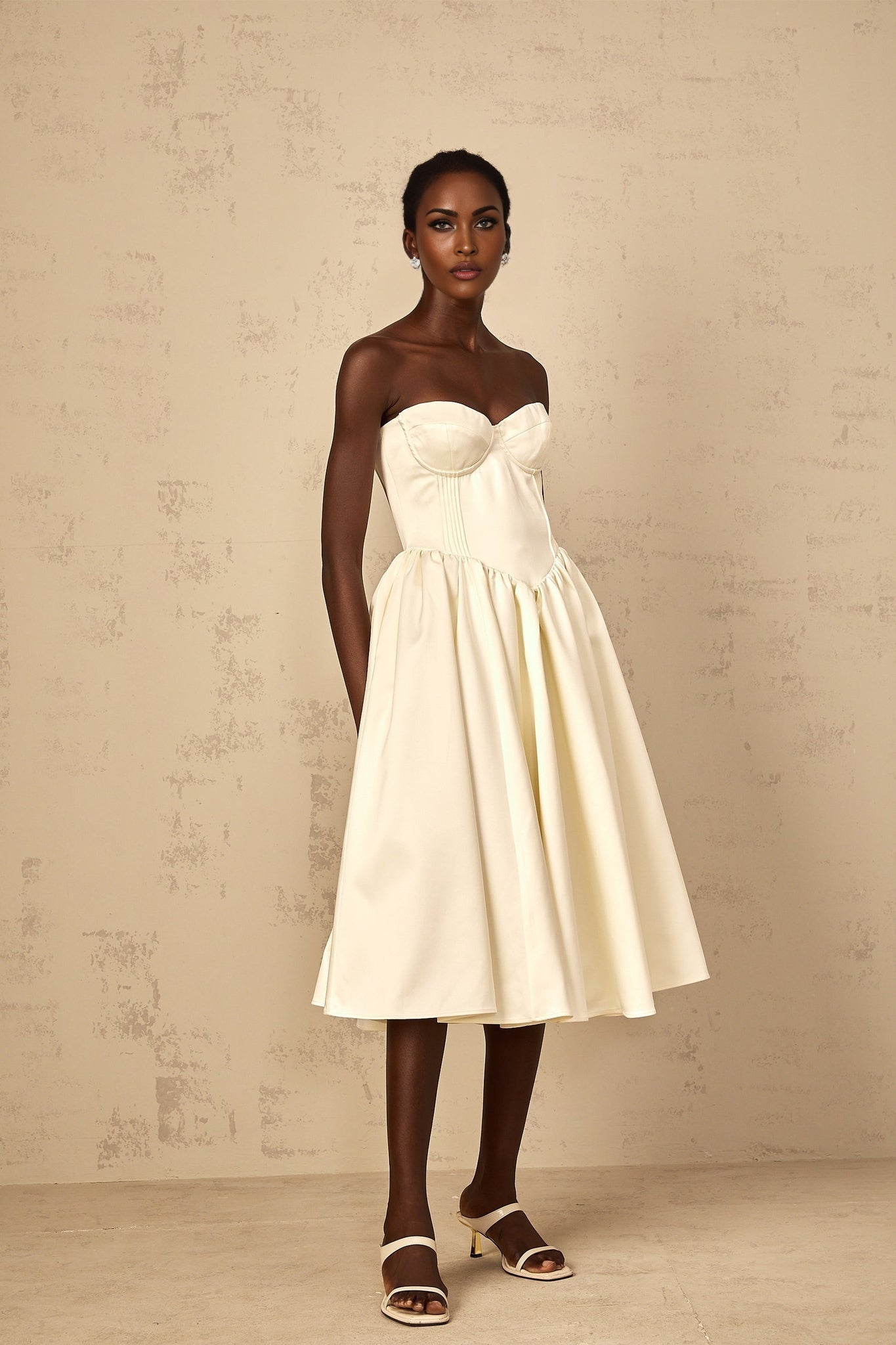 A woman wearing a white offshoulder midi dress with shirred detailing standing in a relaxed pose