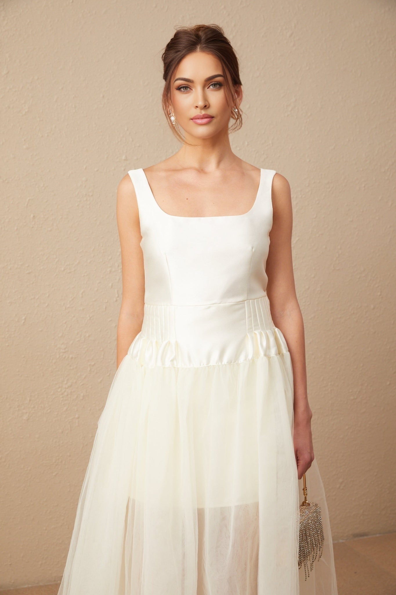 A woman wearing a white satin and tulle maxi dress with panel details standing in an elegant pose