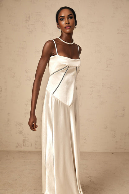 A woman wearing a white satin maxi dress with a flared skirt standing against a plain background