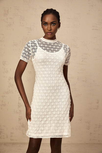 A woman wearing a white semisheer knit mini dress with short sleeves and a formfitting silhouette