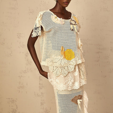 A woman wearing a white sleeveless top with intricate lace panels and crochet knit details