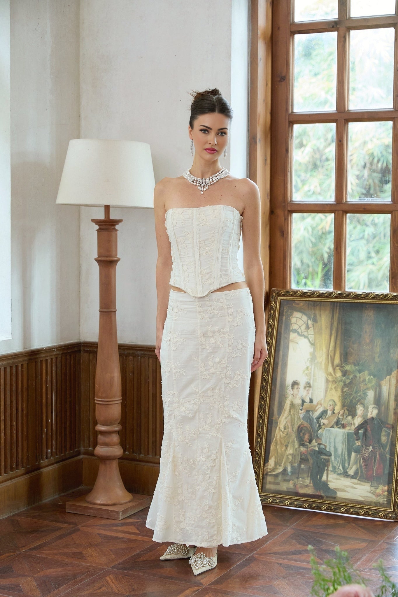 A woman wearing a white twopiece outfit consisting of an embroidered top and matching skirt with delicate floral patterns