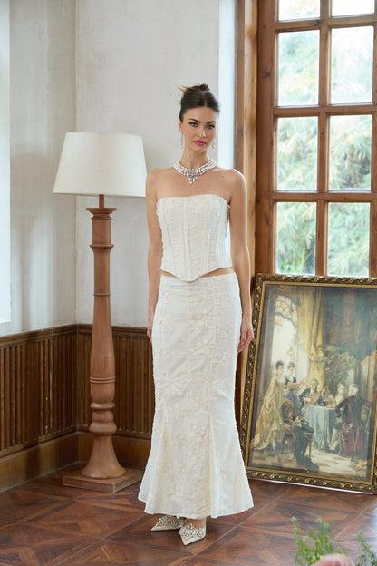 A woman wearing a white twopiece outfit consisting of an embroidered top and matching skirt with delicate floral patterns