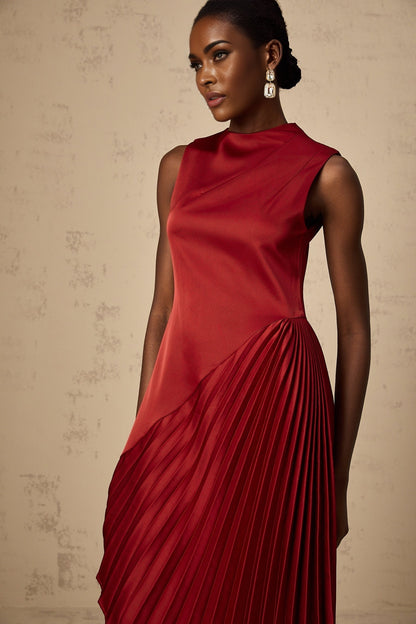 A woman wearing a wine red midi dress with an asymmetric neckline and pleated skirt standing against a plain background