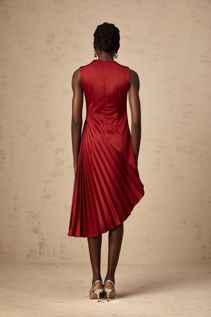 A woman wearing a wine red midi dress with an asymmetric neckline and pleated skirt standing against a plain background