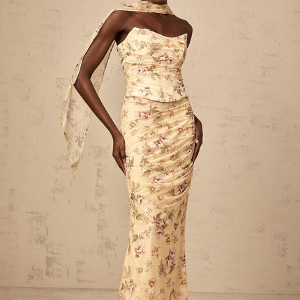 A woman wearing a yellow floral print matching set consisting of a fitted top and skirt standing against a plain background