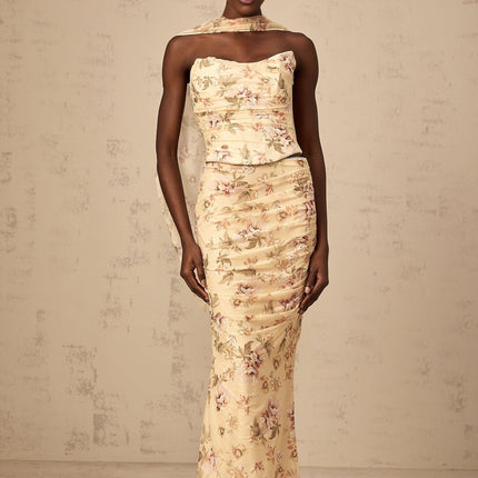 A woman wearing a yellow floral print matching set consisting of a fitted top and skirt with a vibrant summery design