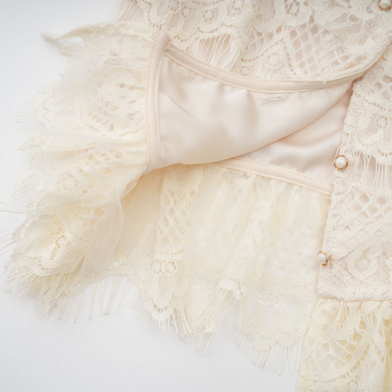 A woman wearing an offwhite blouse with floral lace detailing and a bow accent at the neckline