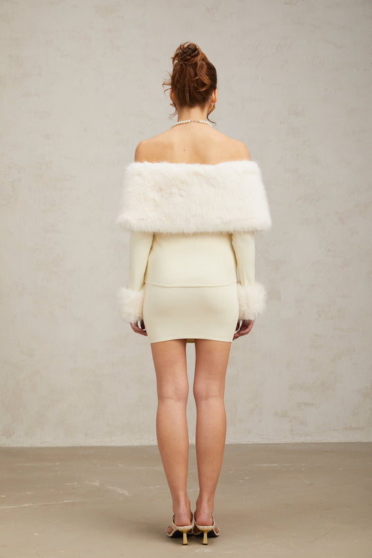 A woman wearing an offwhite matching set consisting of a fineknit top and skirt with faux fur trim