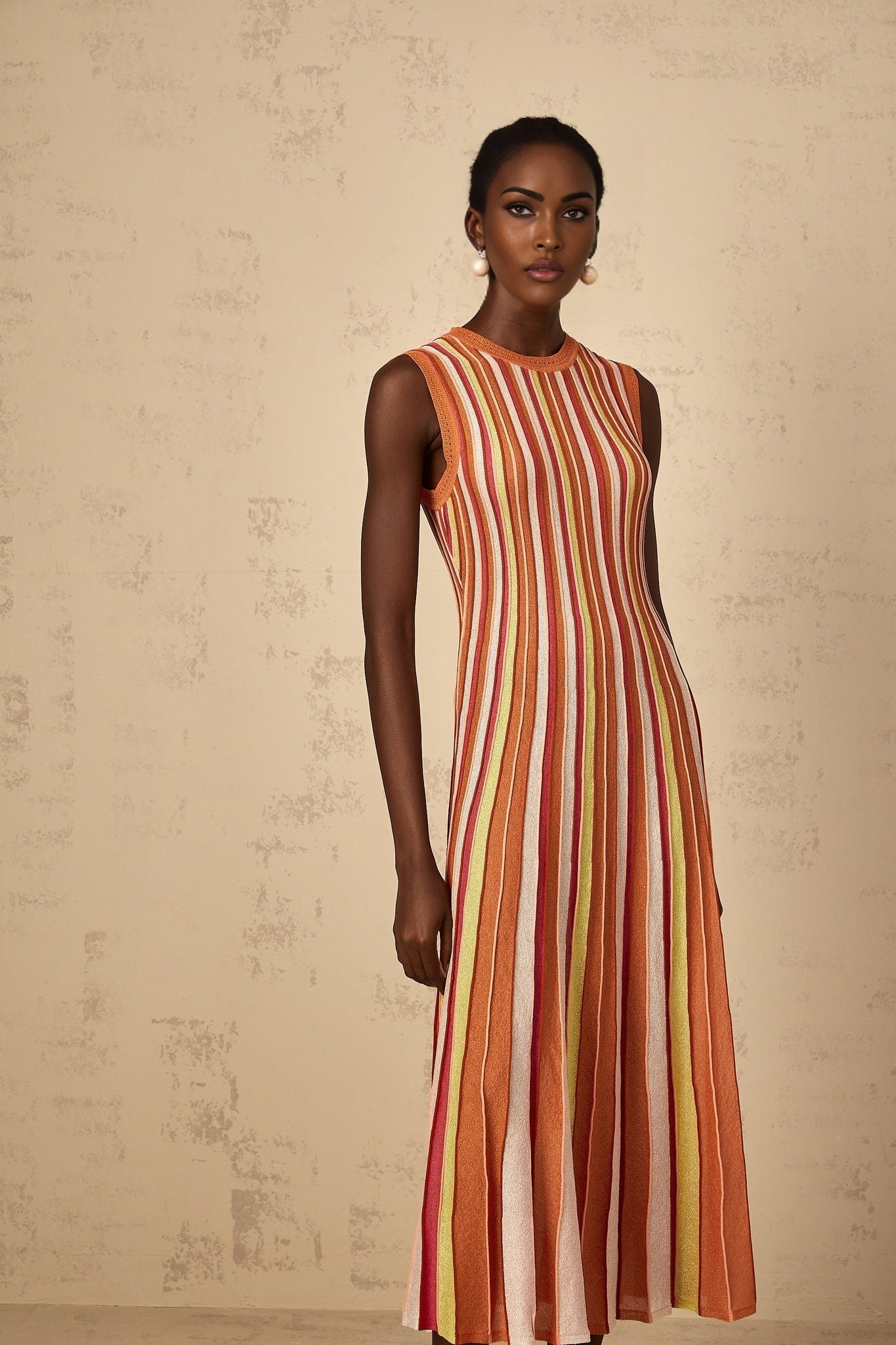 A woman wearing an orange and white vertical striped knit midi dress standing in a neutral background