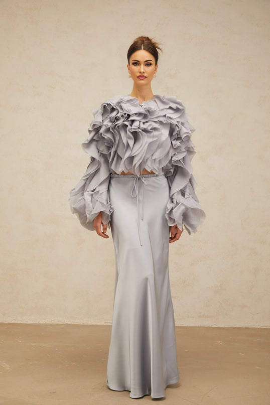 A young girl wearing a light blue blouse with a large bow and ruffled details paired with a matching skirt in the same color creating a coordinated outfit set