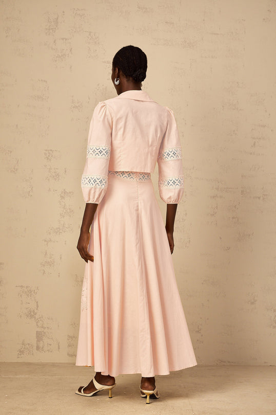 A young girl wearing a pink blouse with floral embroidery paired with a matching dress set The outfit features delicate floral patterns and a feminine design suitable for special occasions