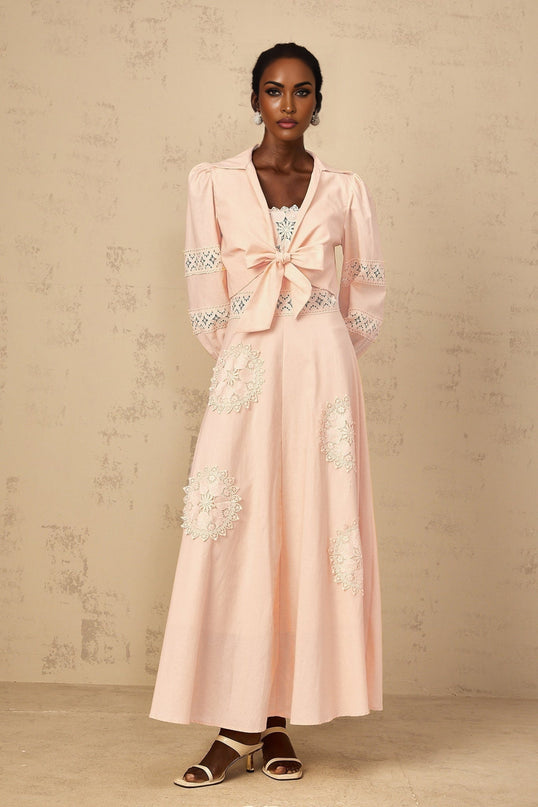 A young girl wearing a pink blouse with floral embroidery paired with a matching dress set The outfit features delicate floral patterns and a soft pink color scheme suitable for a child