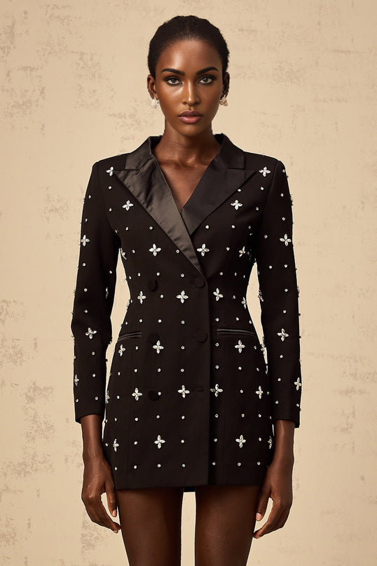 A young woman wearing a black mini blazer dress with crystal embellishments on the lapels and panels standing in a stylish pose against a plain background