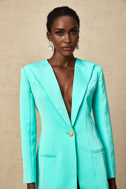 A young woman wearing a green mini blazer dress with a cinched waist the dress features lapels and buttons like a blazer but is styled as a short dress