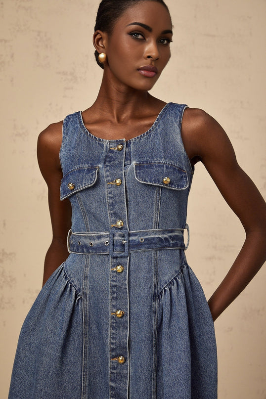 A young woman wearing a light blue denim mini dress with a belt cinched at the waist standing in a casual pose