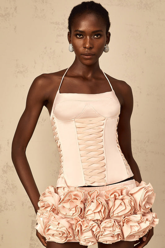 A young woman wearing a pink matching set consisting of a lace up top and skirt adorned with faux flower details
