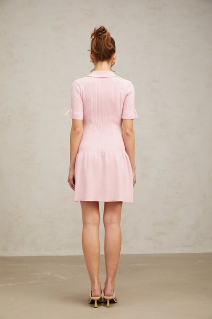 A young woman wearing a pink mini dress with a flared skirt and long sleeves made from fine knit fabric