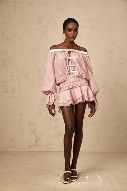 A young woman wearing a pink offshoulder mini dress with a bow detail and flounced hem