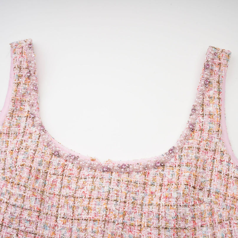 A young woman wearing a pink tweed mini dress with embellishments standing in a neutral background