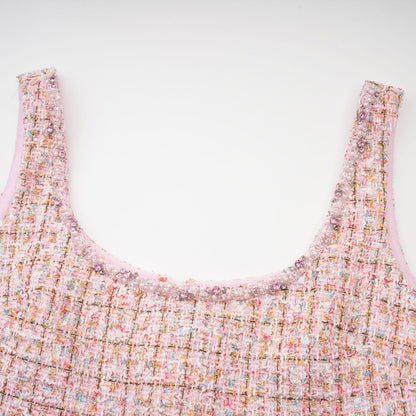 A young woman wearing a pink tweed mini dress with embellishments standing in a neutral background