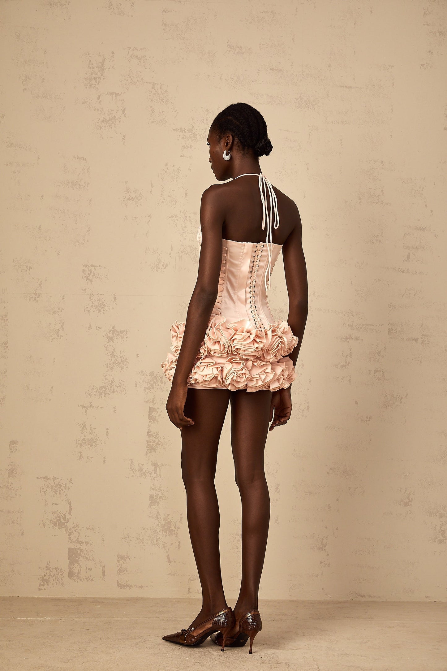 A young woman wearing a pink twopiece outfit consisting of a laceup top and matching skirt decorated with faux flowers