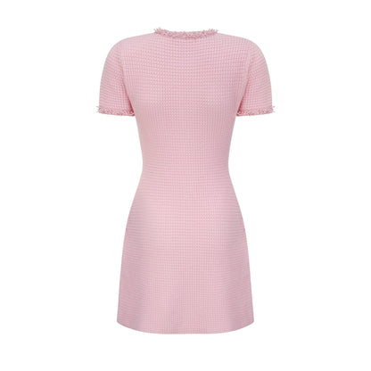A young woman wearing a short pink knitted dress with beaded embellishments standing against a plain background