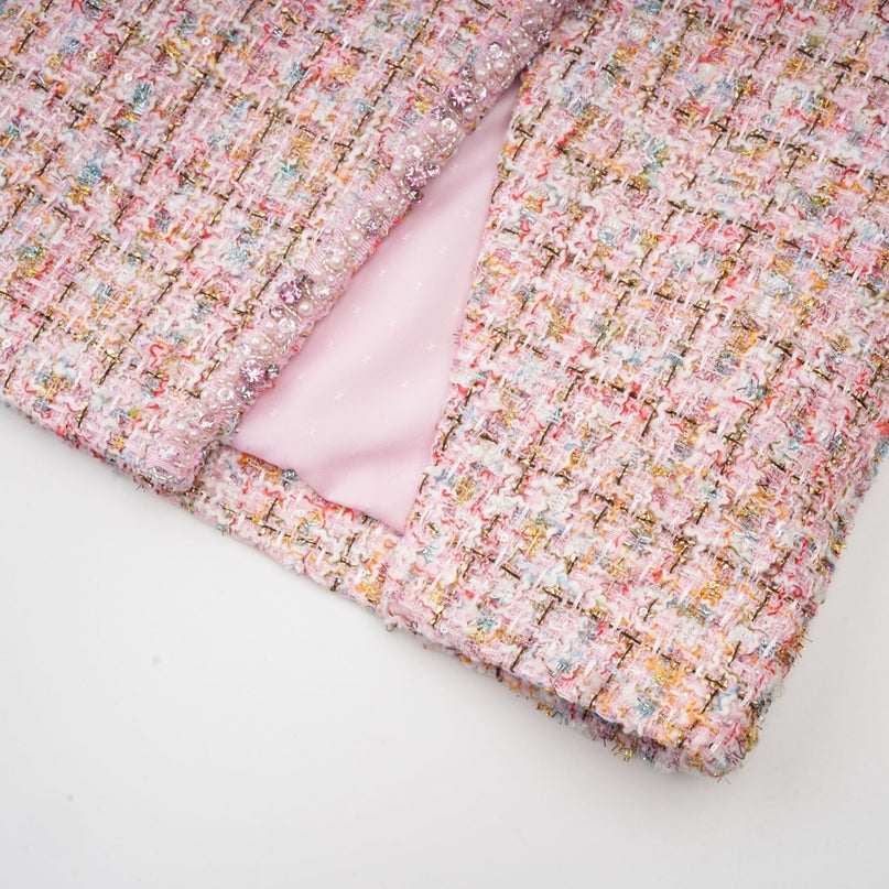 A young woman wearing a short pink tweed dress with embellishments standing against a plain background