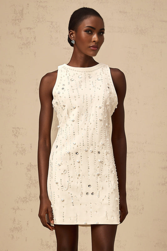 A young woman wearing a short white Aline dress with embellishments standing in a neutral studio setting