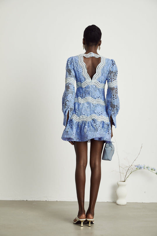 A young woman wearing a short white mini dress with a Vneckline and colorful floral embroidery standing in a casual pose against a plain background