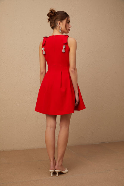 A young woman wearing a vibrant red sleeveless mini dress with a pleated skirt and a large bow detail at the neckline