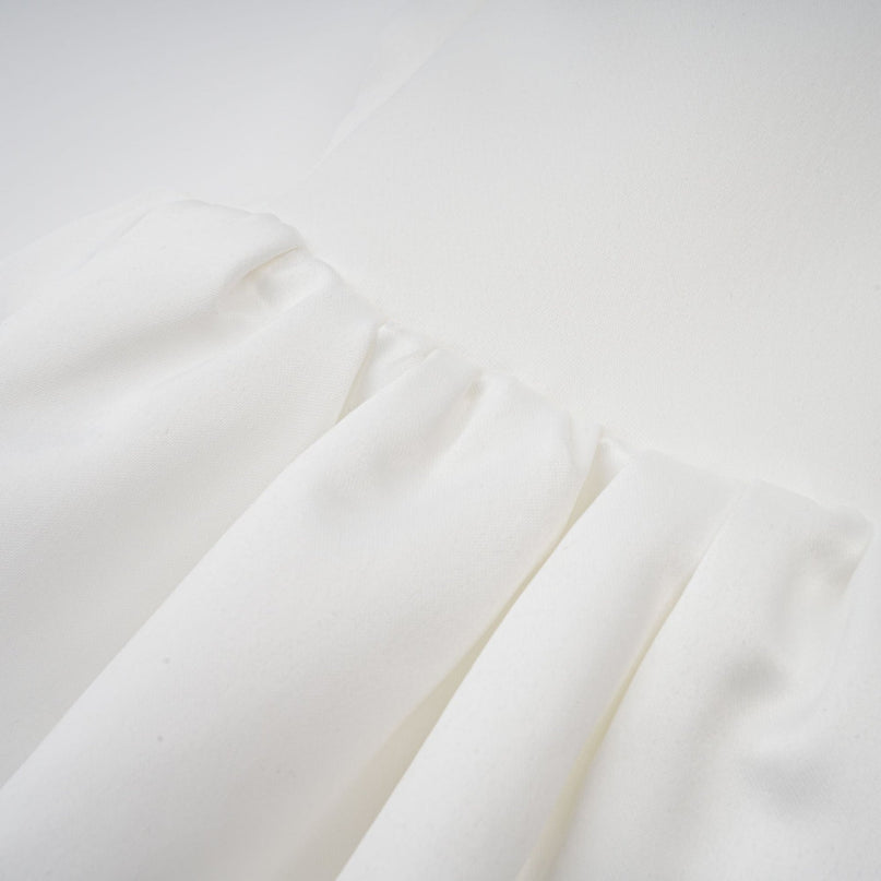 A young woman wearing a white halterneck mini dress with ruffle details standing against a plain background