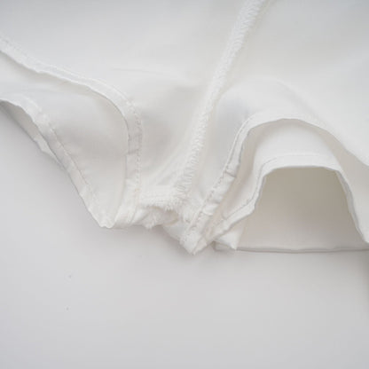 A young woman wearing a white halterneck mini dress with ruffled details standing against a plain background