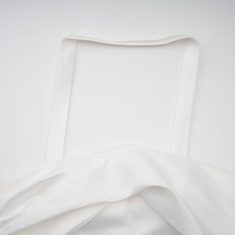 A young woman wearing a white halterneck mini dress with ruffled details standing against a plain background