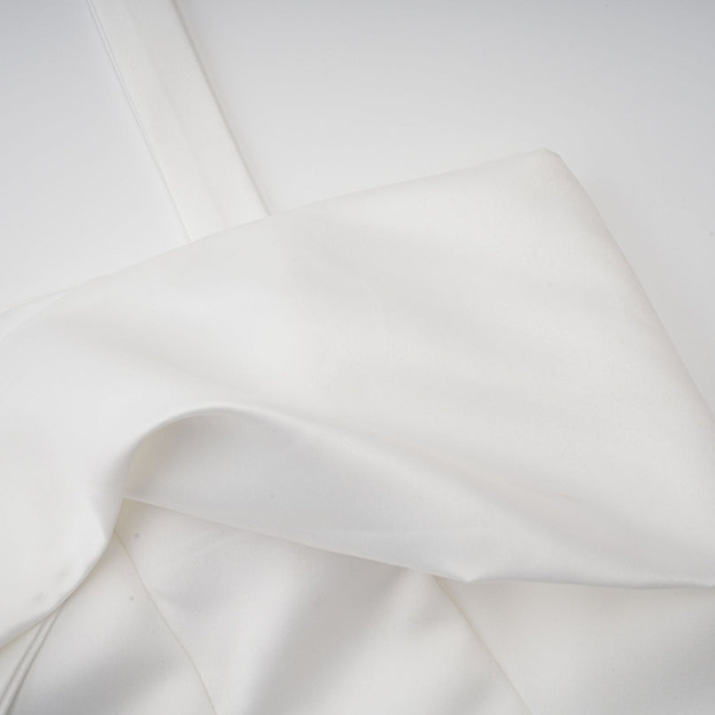 A young woman wearing a white halterneck mini dress with ruffled details standing in a casual pose