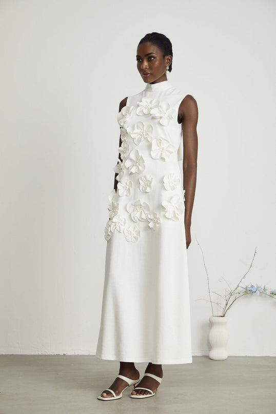 Alt text Woman wearing a white sleeveless maxi dress with bow detail and decorative artificial flowers