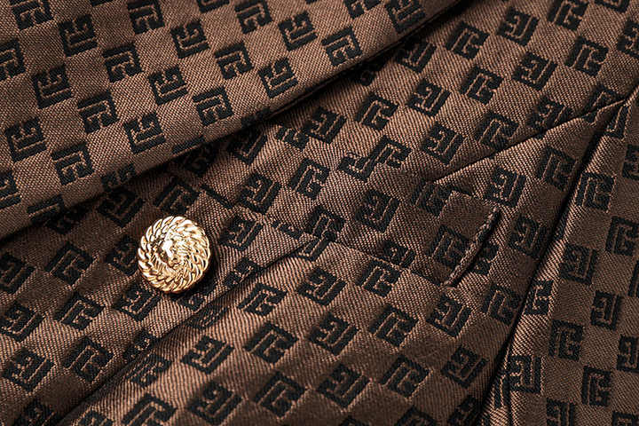 April wearing a tailored double-breasted brown blazer with gold buttons and embossed geometric design