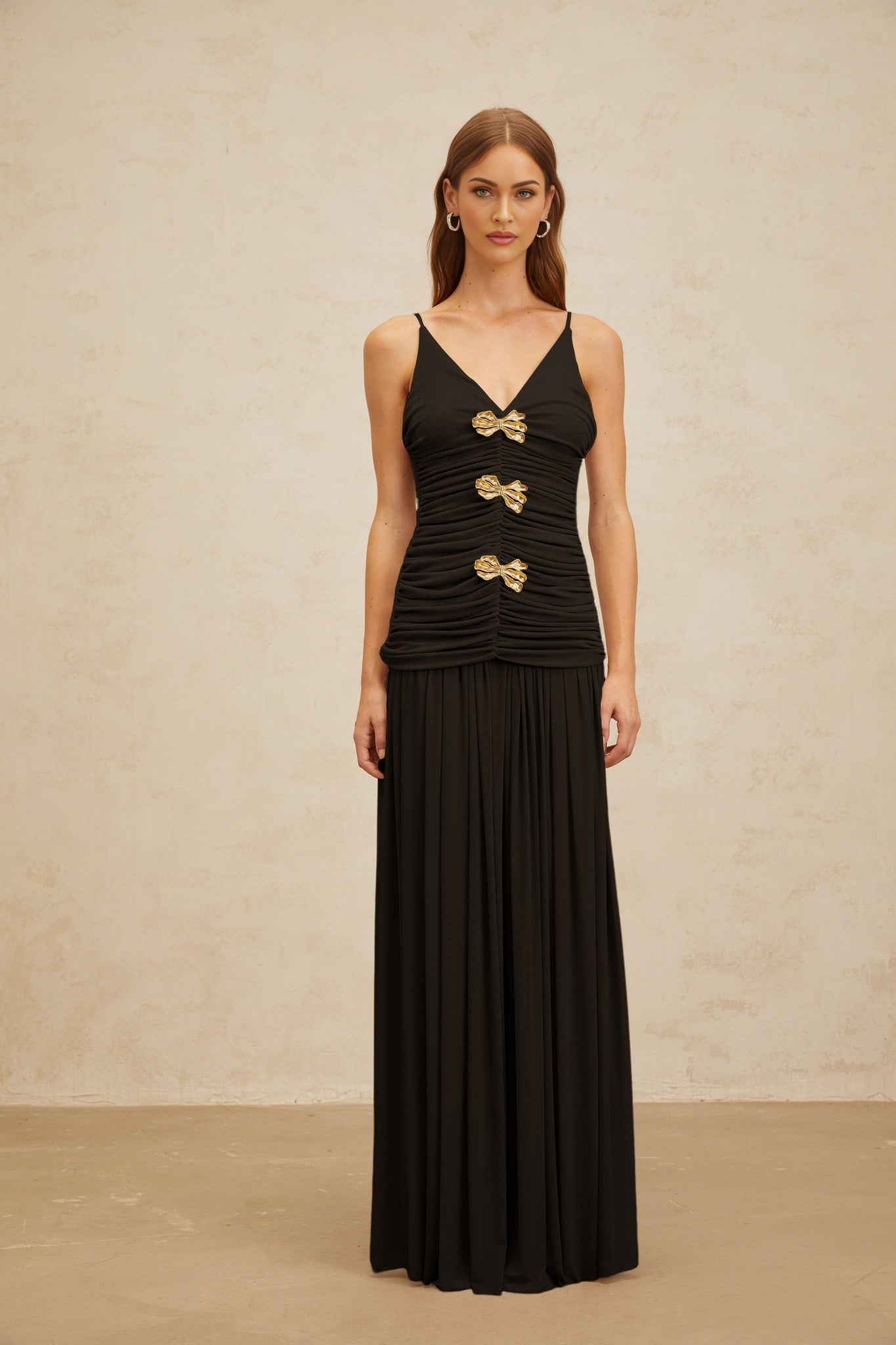 Black V-neck sleeveless top with brooch and ruched detailing, adjustable spaghetti straps and rear zip fastening, paired with black pleated maxi skirt with rear zip fastening