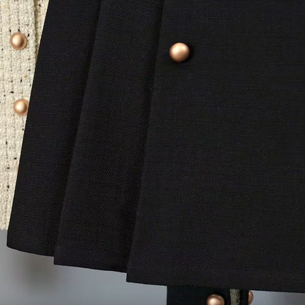 White tweed jacket with pearl buttons and contrasting cuffs, paired with a pleated black high-waisted skirt