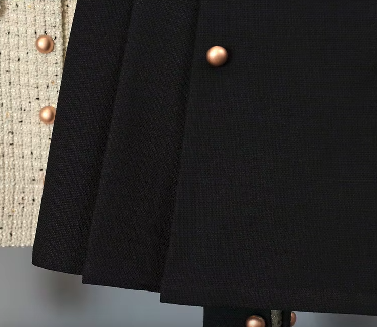 White tweed jacket with pearl buttons and contrasting cuffs, paired with a pleated black high-waisted skirt