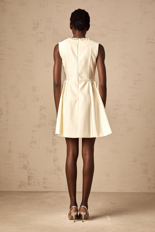 Delizia Mini Dress in Ivory White with Faux-pearl embellishment Sleeveless Bowknot Pleat Flared skirt Crew neck Rear zip fastening Thigh-length 41% Elastane 38% Cotton 12% Acetate 9% Wool