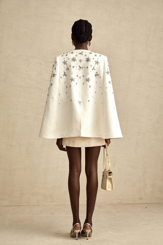 Elegant white jacket with cape design featuring intricate embellishments and delicate beadwork