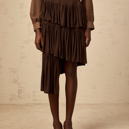 Emma wearing Brown Liora Pleated Tiered Mini Skirt with asymmetrical hem and draped detailing in luxurious Terylene fiber and Spandex blend