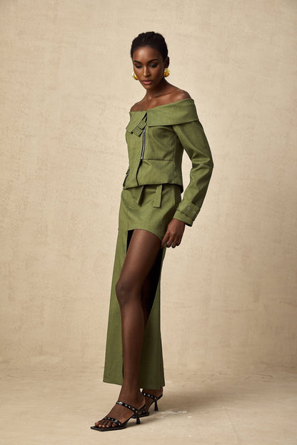 Green asymmetric jacket and matching skirt set worn by model standing against plain background